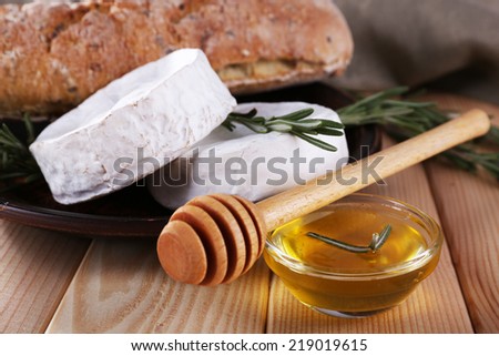Camembert cheese on plate, bread, honey in glass bowl and napkin on wooden background