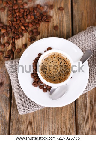 Cup of coffee with milk and coffee beans on napkin on wooden background