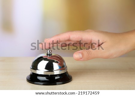 Female hand ring bell on  hotel reception desk, on bright background