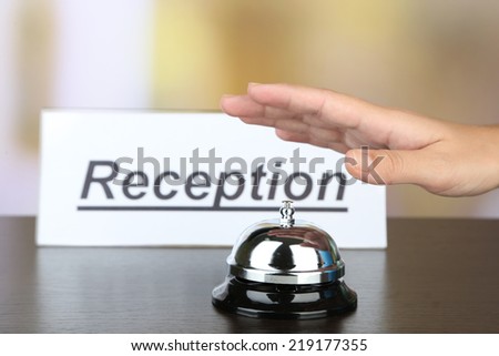 Female hand ring bell on  hotel reception desk, on bright background
