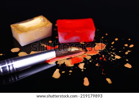 Watercolor paint cubes with brushes and spilled paint isolated on black