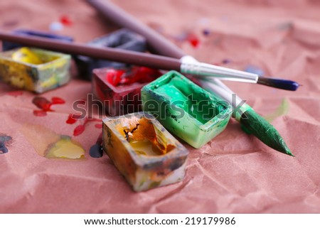 Watercolor paint cubes with brushes and spilled paint on brown paper background