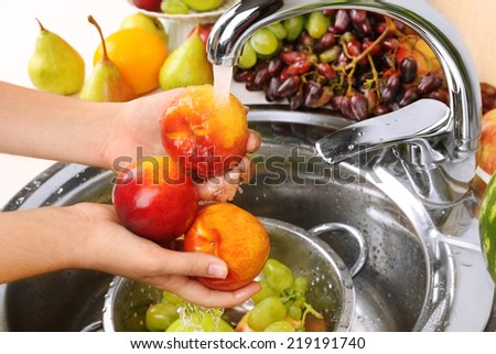 Woman\'s hands washing peaches and other fruits in colander in sink