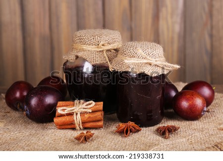 Tasty plum jam in jars and plums on wooden table on wooden background