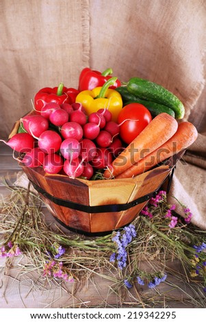 Big round wooden basket with vegetables on sacking background