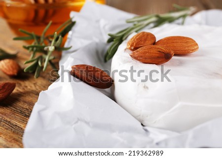 Camembert cheese on paper, honey in glass bowl and nuts close up