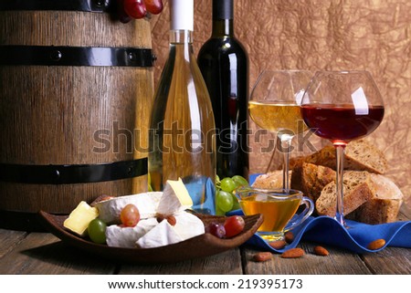 Supper consisting of Camembert and Brie cheese, honey, wine and grapes on napkin in basket and wine barrel on wooden table on brown background
