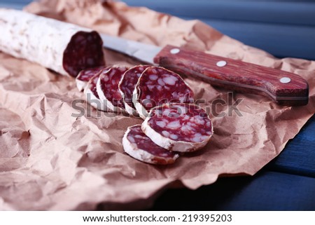 French salami and knife on craft paper on dark blue wooden background