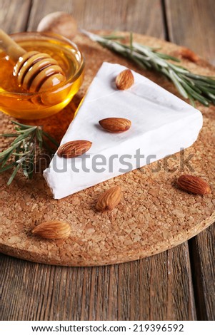 Brie cheese, honey in glass bowl and nuts on wooden background