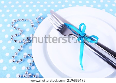White plate, fork, knife and Christmas decoration on polka dot tablecloth closeup