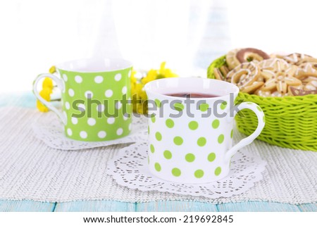 Two polka dot cups of tea with biscuits on table on curtain background