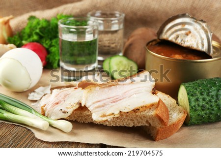 Bacon, fresh vegetables, boiled egg and bread on paper, glasses with vodka on wooden background. Village breakfast concept.