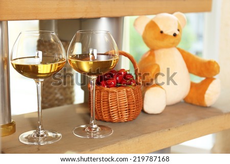 Teddy bear with wine glasses on shelf in room