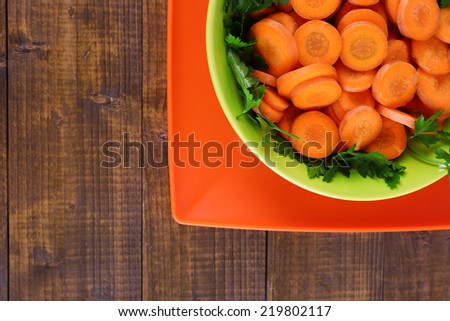 Slices of carrot, sorrel and parsley in green round bowl on wooden background