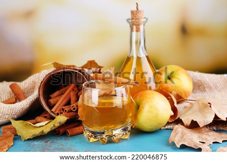 Composition of apple cider with cinnamon sticks, fresh apples and autumn leaves on wooden table, on bright background
