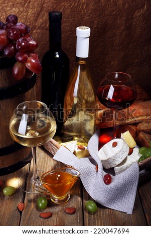 Supper consisting of Camembert and brie cheese, honey, wine and grapes on napkin in basket and wine barrel on wooden table on brown background