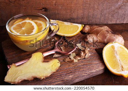 Cup of ginger drink with lemon on cutting board on wooden table on wooden wall background