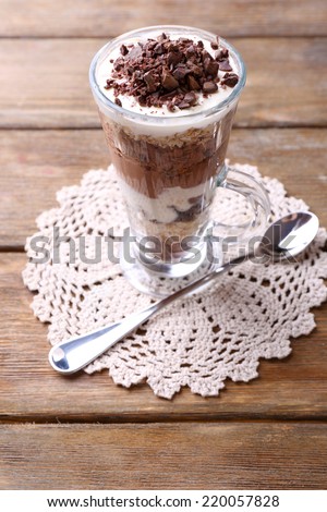 Yogurt, with chocolate cream, chopped chocolate and muesli served in glass on wooden background