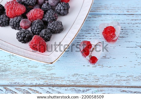 Ice cubes with red currant and frozen forest berries on plate, on wooden background