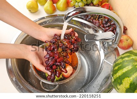 Woman\'s hands washing grapes and other fruits in colander in sink