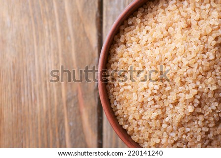 Brown crystal sugar in bowl on wooden background