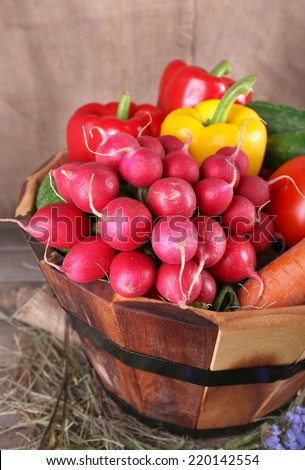 Big round basket with dried grass, vegetables and fresh eggs on sacking background