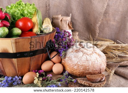 Big round wooden basket with vegetables, milk and bread on sacking background
