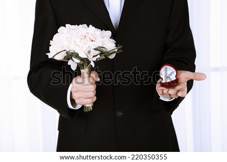 Man holding wedding bouquet and ring on light background