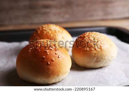 Tasty buns with sesame on oven-tray, on wooden background