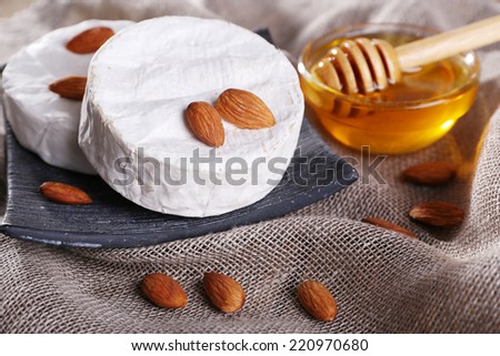 Camembert cheese on plate, honey in glass bowl and nuts on sackcloth background