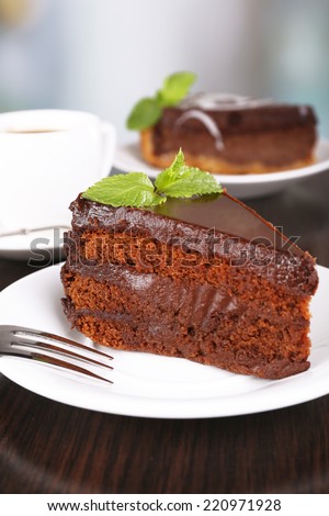 Pieces of chocolate cake on plates and cup of tea on wooden table on natural background