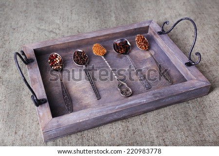 Seasonings in metal spoons on wooden tray on fabric background