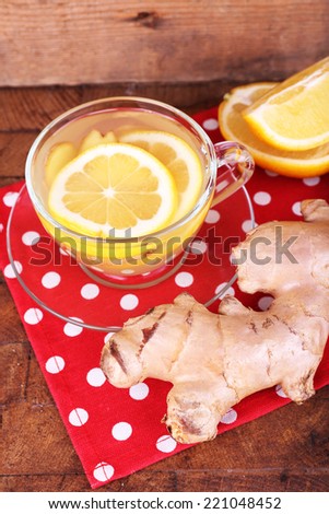 Cup of ginger drink with lemon on polka dot napkin on wooden table on wooden wall background