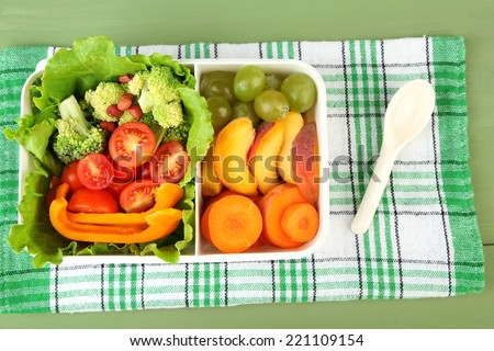 Tasty vegetarian food in plastic box on green wooden table