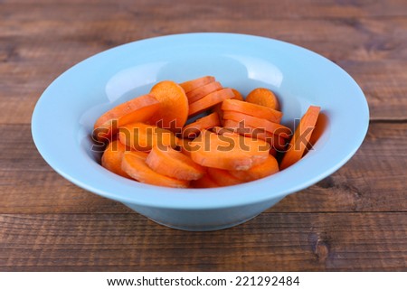 Slices of carrot in blue round bowl on wooden background