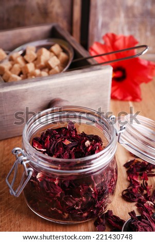 Dried hibiscus tea in glass jar, fresh hibiscus flower and brown sugar in box, on wooden background