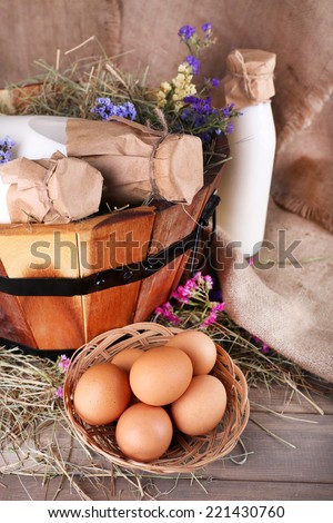 Big round basket with dried grass, milk and fresh eggs on sacking background