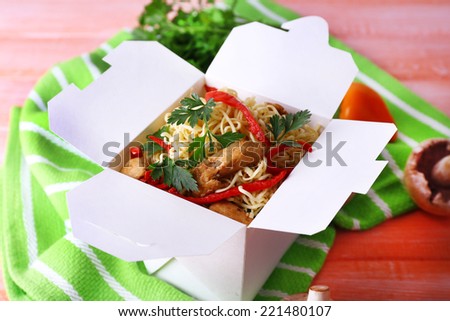 Chinese noodles in takeaway box on green napkin on pink background