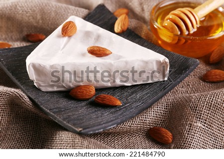 Brie cheese, honey in glass bowl and nuts on sackcloth background