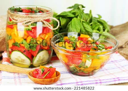 Vegetable salad in glass jar and bowl on wooden table, on bright background