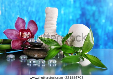 Spa composition with herbal massage bags, orchid and bamboo on table on blue background