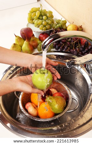 Woman\'s hands washing apple and other fruits in colander in sink