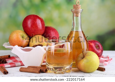 Apple cider  in bottle  with cinnamon sticks and fresh apples on wooden table, on bright background