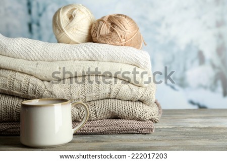 Cup of hot drink, knitting clothes and yarn on light winter background