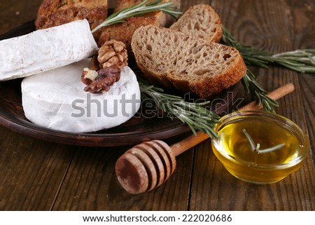 Camembert cheese on plate, honey, nuts and bread on wooden background