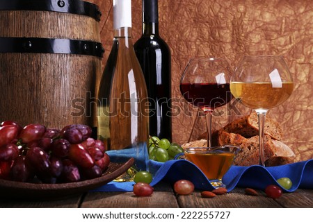 Supper consisting of Camembert and Brie cheese, honey, wine and grapes on napkin in basket and wine barrel on wooden table on brown background