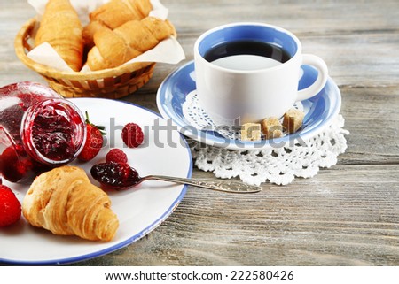 Breakfast with tea, raspberry jam and fresh croissants on wooden background