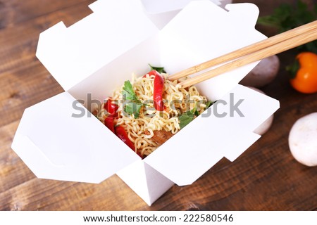 Chinese noodles in takeaway boxes with mushrooms and parsley on wooden background
