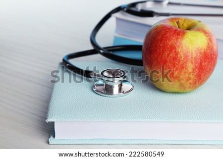Medical stethoscope with apple on books on wooden table