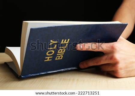 Male hands with Bible on wooden table on dark background